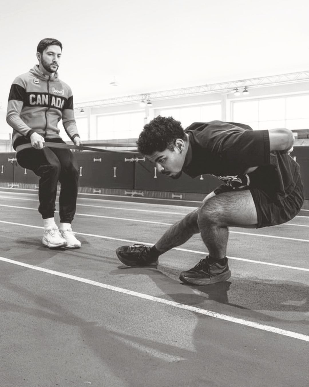 Athlete training on a track, performing resistance exercises with a coach using a resistance band for added strength development.